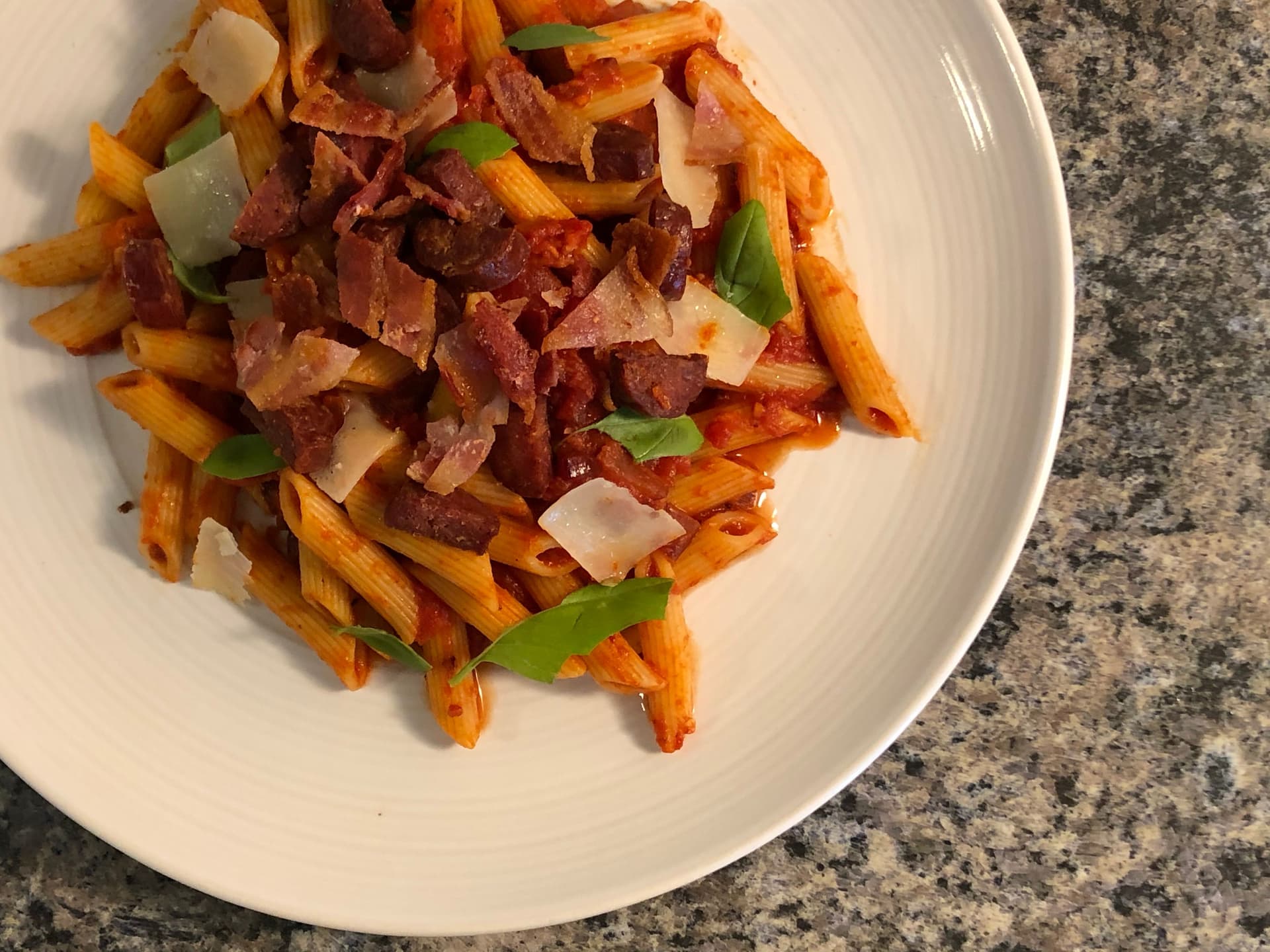 Spicy bacon and chorizo pasta with diced onions and green peppers on a white plate.