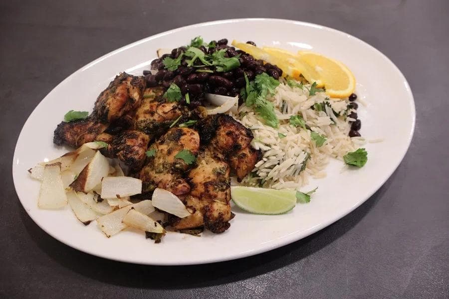 Plated Cuban mojo chicken with rice, black beans, onions, cilantro, and lime wedge on white plate.