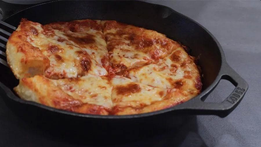 Golden-brown cast iron skillet pizza with melted cheese and crispy edges, ready to serve.