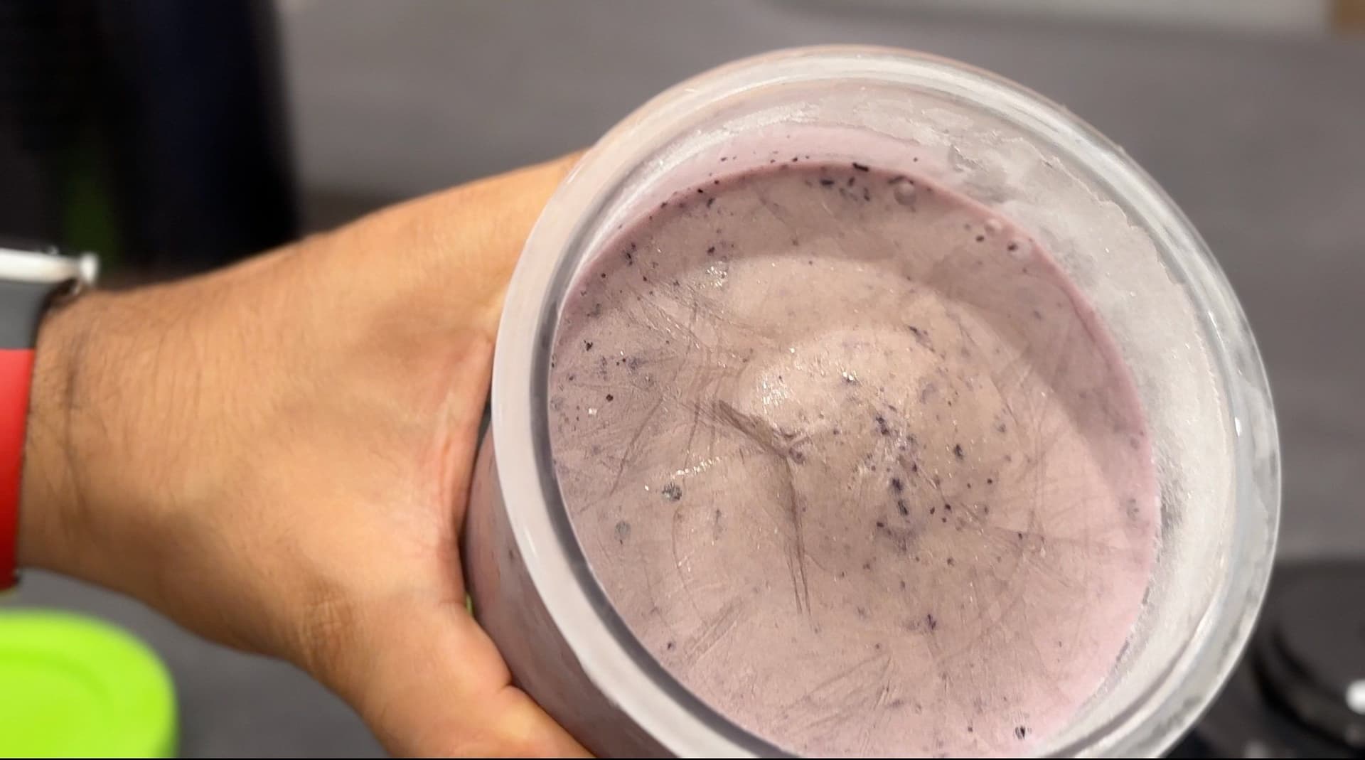 Hand holding a Ninja Creami jar filled with frozen blueberry cheesecake protein ice cream mixture before processing.