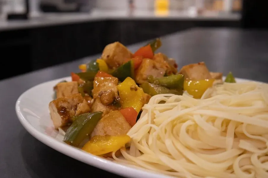 Crispy tofu stir fry with bell peppers and green beans served over noodles on a white plate.