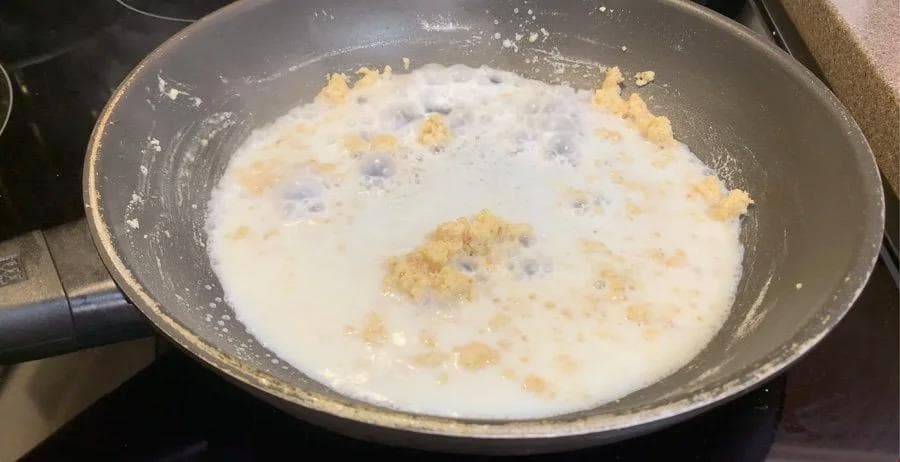Creamy white béchamel sauce simmering in a pan with visible butter and flour roux particles.