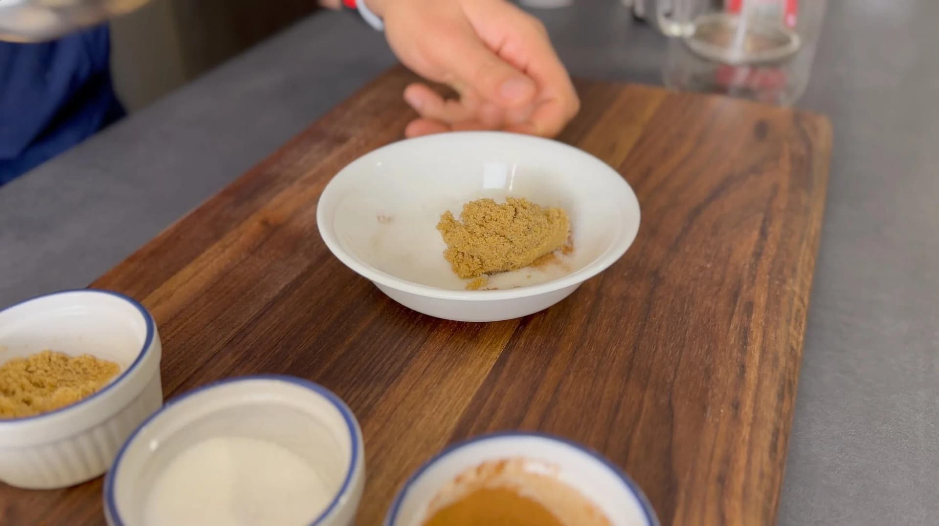 Cinnamon sugar mixture in white bowl on wooden board with other ingredients nearby during preparation.