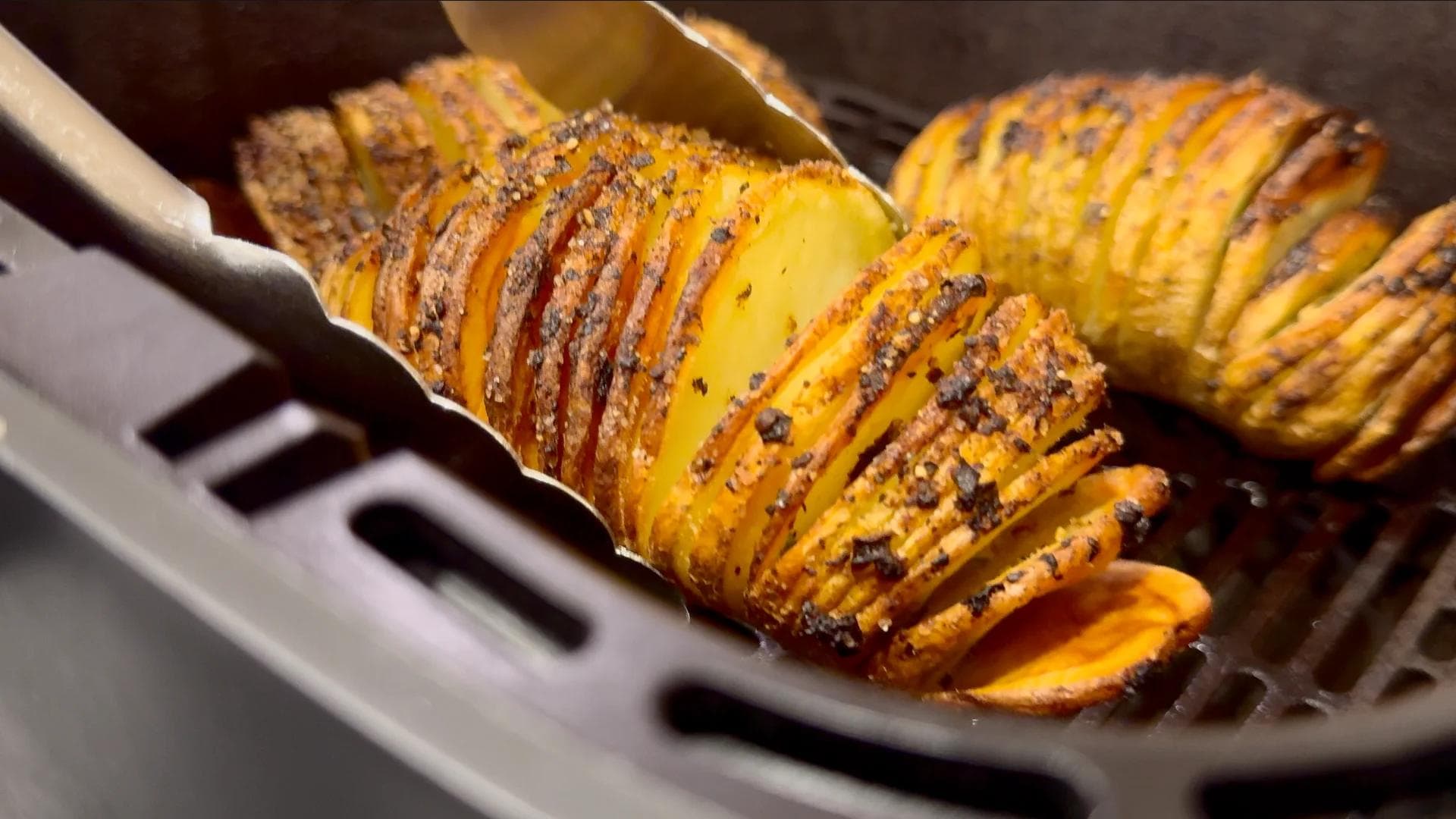 Crispy golden hasselback potatoes with seasoning in an air fryer basket, sliced and caramelized.