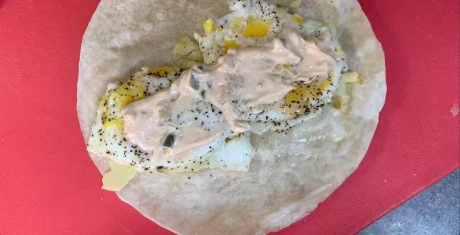 Assembled breakfast wrap with eggs, cheese, hash brown, and seasoning on a tortilla before wrapping.
