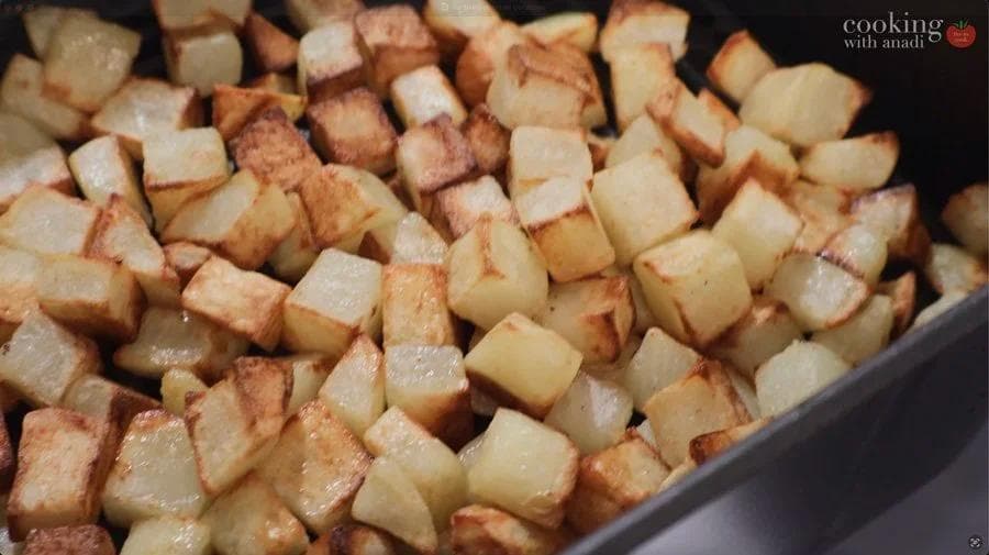 Golden and crispy air fried potato cubes in a dark cooking basket, partially cooked and glistening.