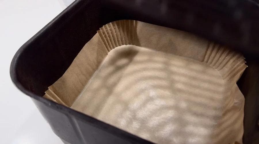 Air fryer basket lined with parchment paper, ready for cooking tandoori chicken.
