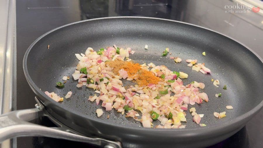 Diced onions, ham, and green peppers sautéing in a black pan with turmeric and spices on the stovetop.