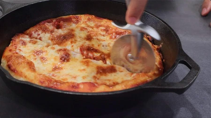 Golden-brown cast iron skillet pizza with melted mozzarella cheese and crispy crust being sliced.