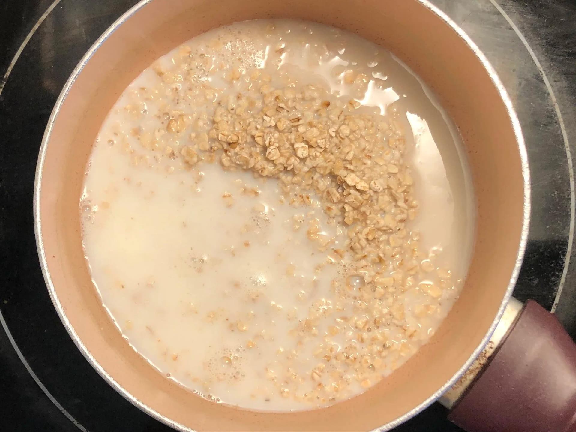 Oats and milk simmering in a pot with a cream-colored liquid and tan oat pieces visible.