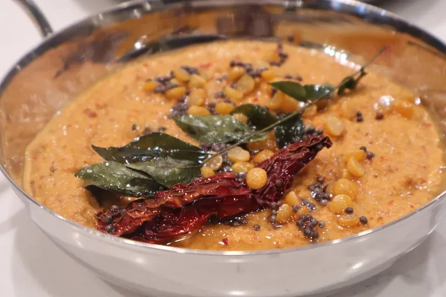 South Indian roasted peanut chutney garnished with curry leaves, dried red chilies, and mustard seeds in a white bowl.