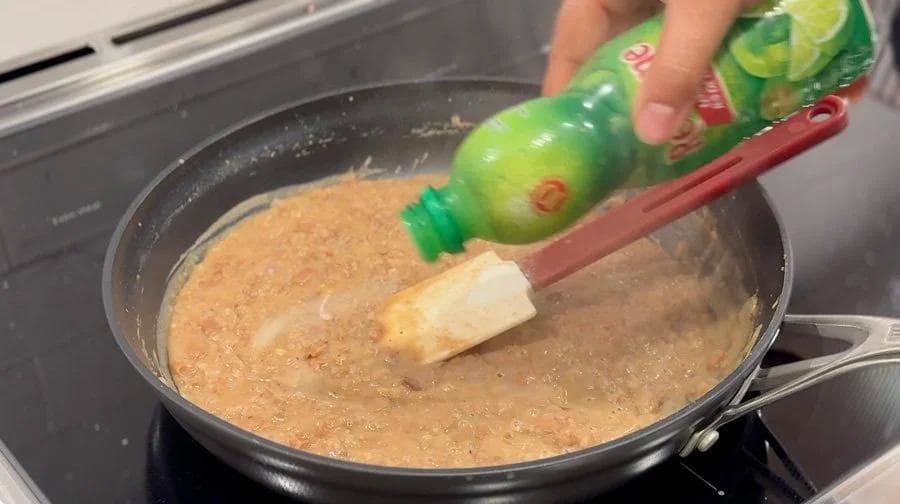 Lime juice being squeezed into a pan of mashed refried beans on the stovetop.