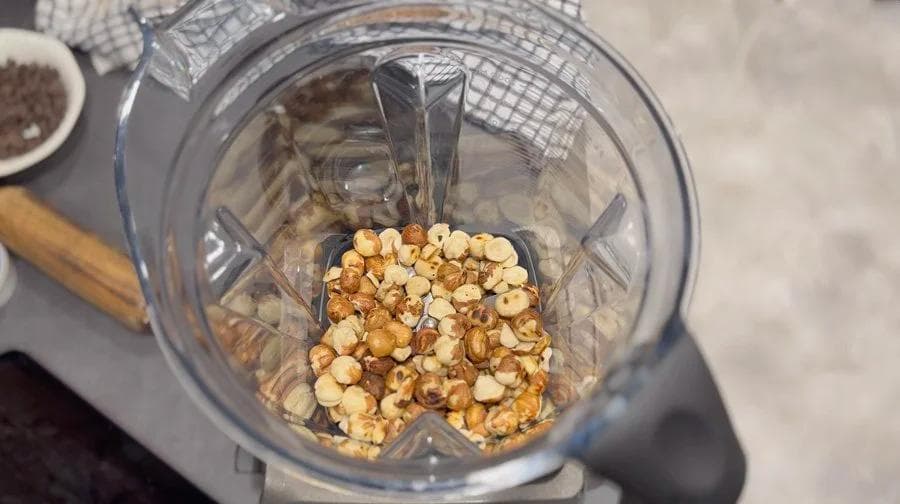 Hazelnuts being processed in a food processor to create a fine, crumbly texture for homemade nutella.