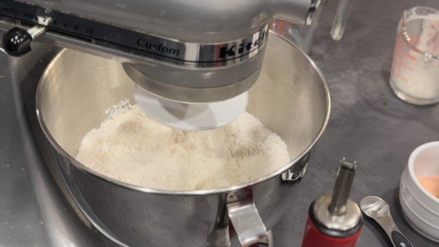 Flour being mixed in a stand mixer bowl during pizza dough preparation.
