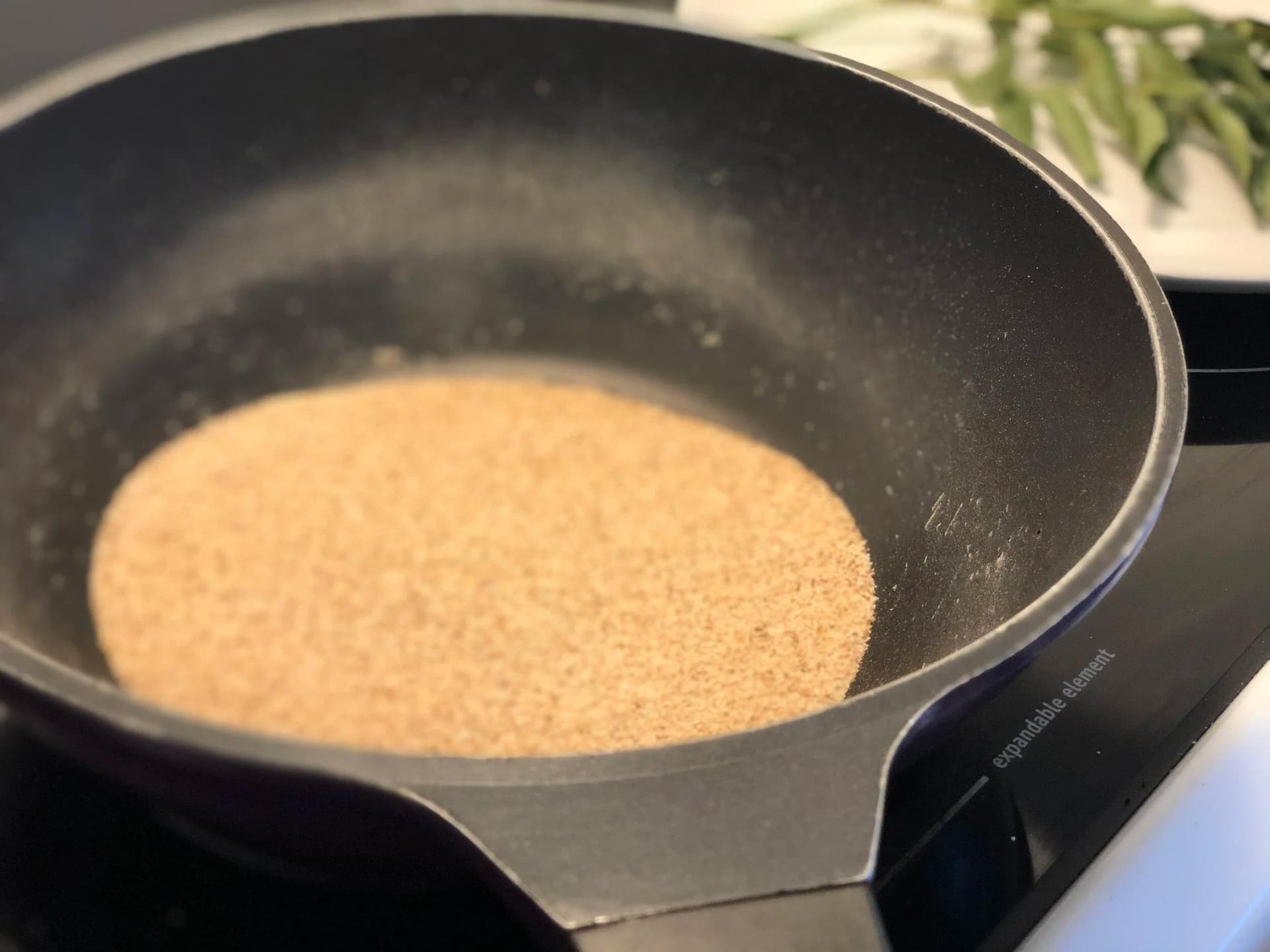 Semolina being roasted in a dark pan on a stovetop, showing light golden color from toasting.