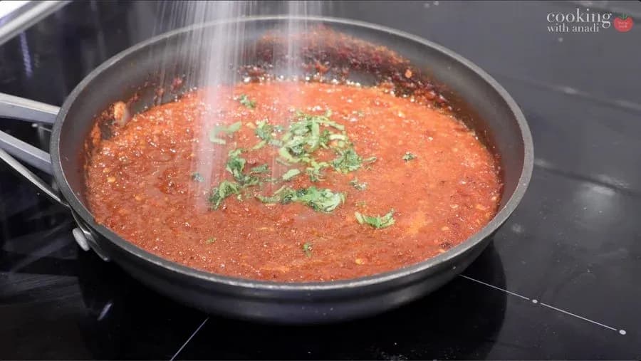 Simmering salsa roja in a pan topped with fresh cilantro garnish