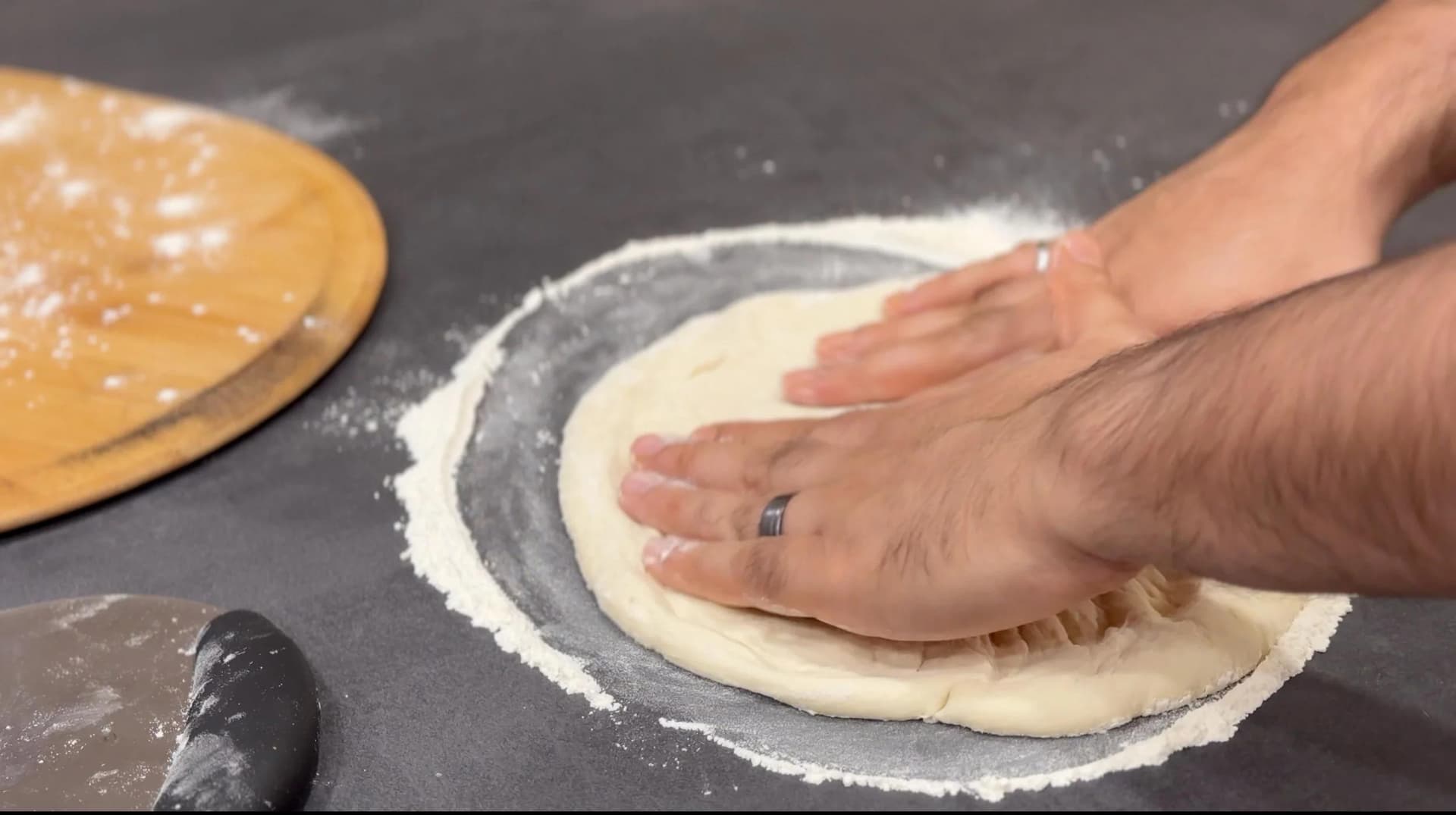 Hands stretching pizza dough on a floured surface with finished dough rounds nearby.