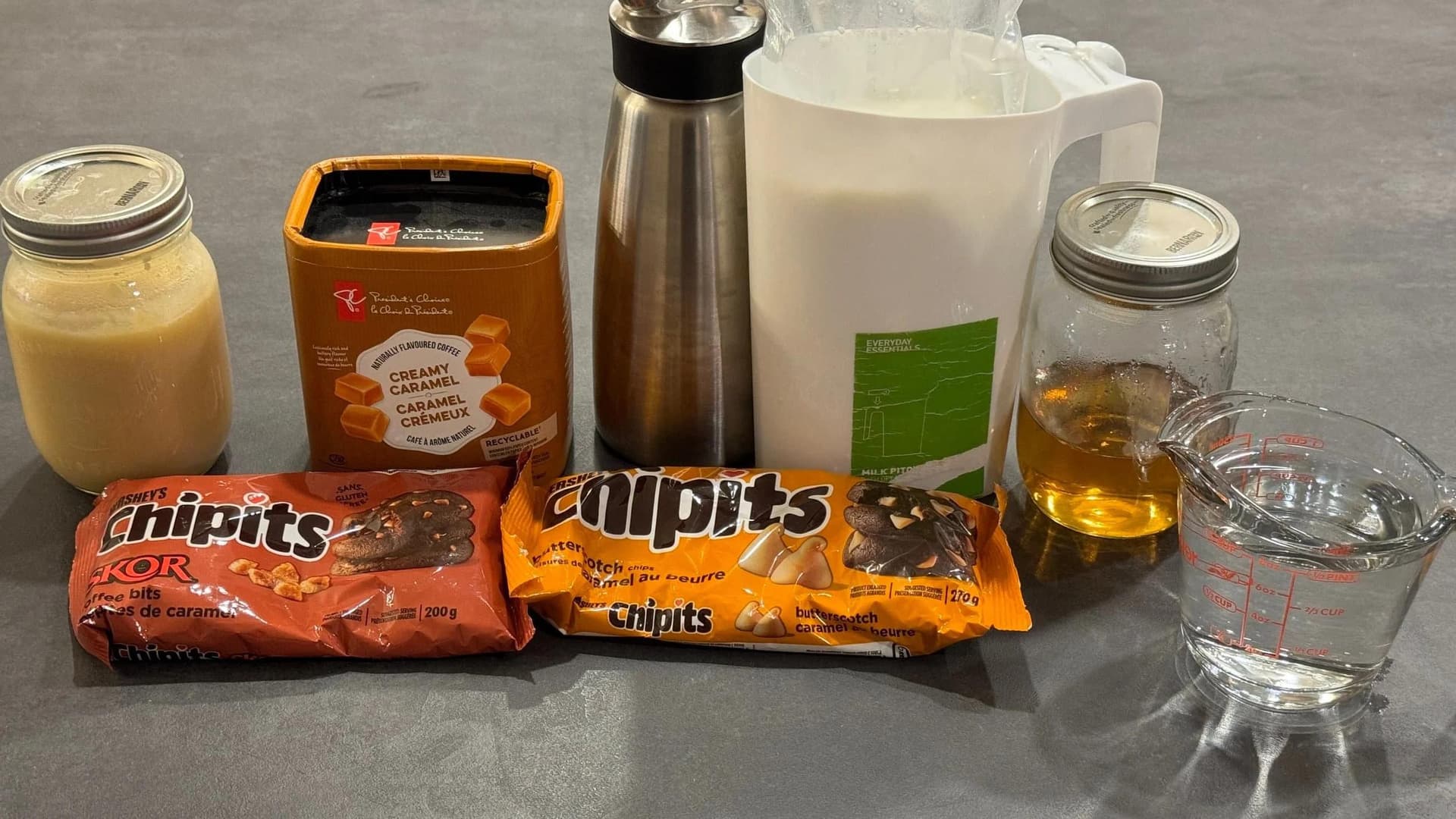 Ingredients for Caramel Brulee Latte laid out on a counter including Baileys, creamer, milk, oil, water, and Calpis drinks.