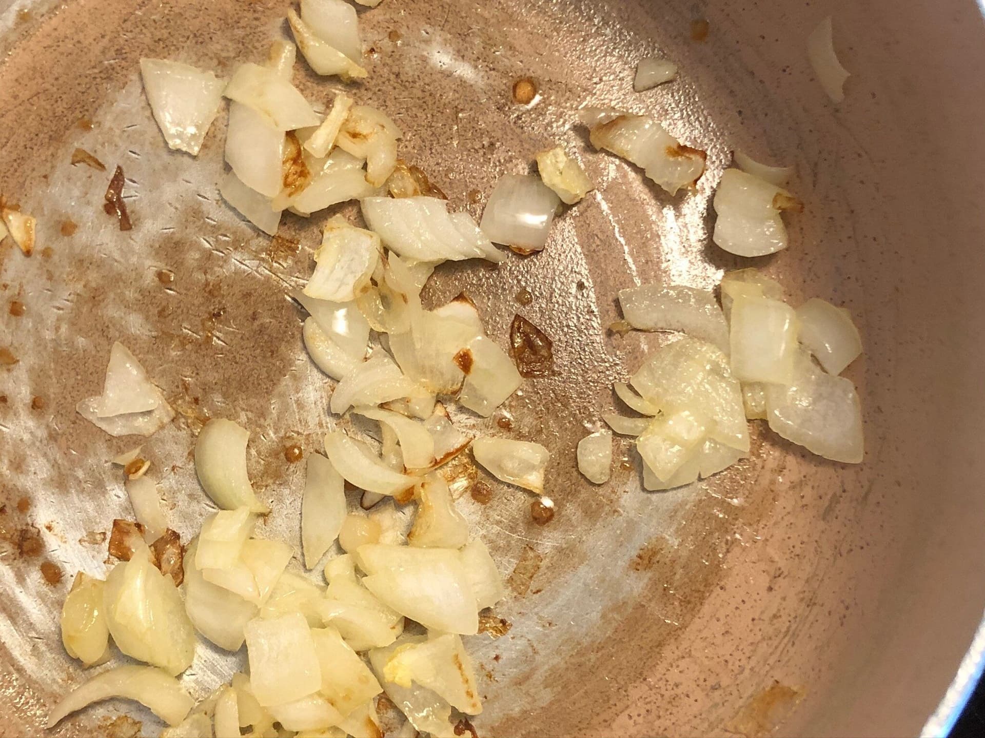 Diced onions being sautéed in olive oil in a pot until translucent and soft.