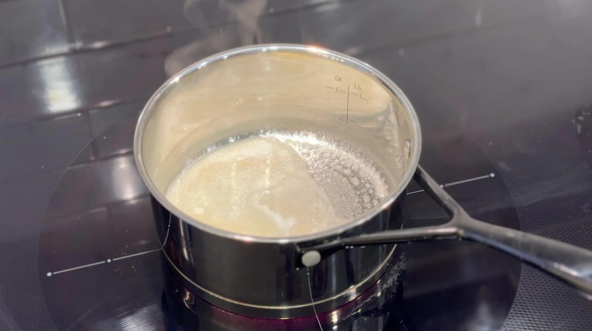 Milk being whisked into a roux in a saucepan to make béchamel sauce for potato gratin.