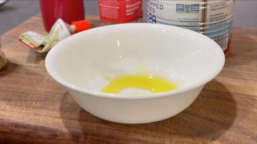 Olive oil mixed in a white bowl for pizza sauce, with ingredients and bottles in the background.