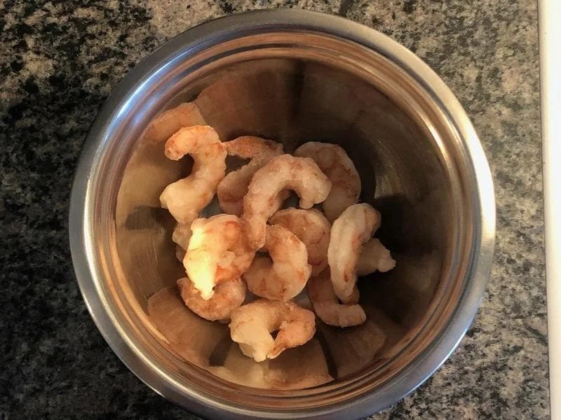 Frozen shrimp partially defrosted in a stainless steel bowl on a granite countertop.