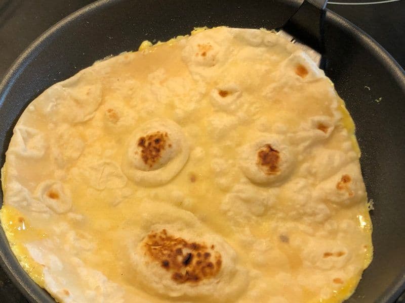 Egg paratha cooking in a dark pan with golden-brown spots, partially cooked eggs visible on the surface.