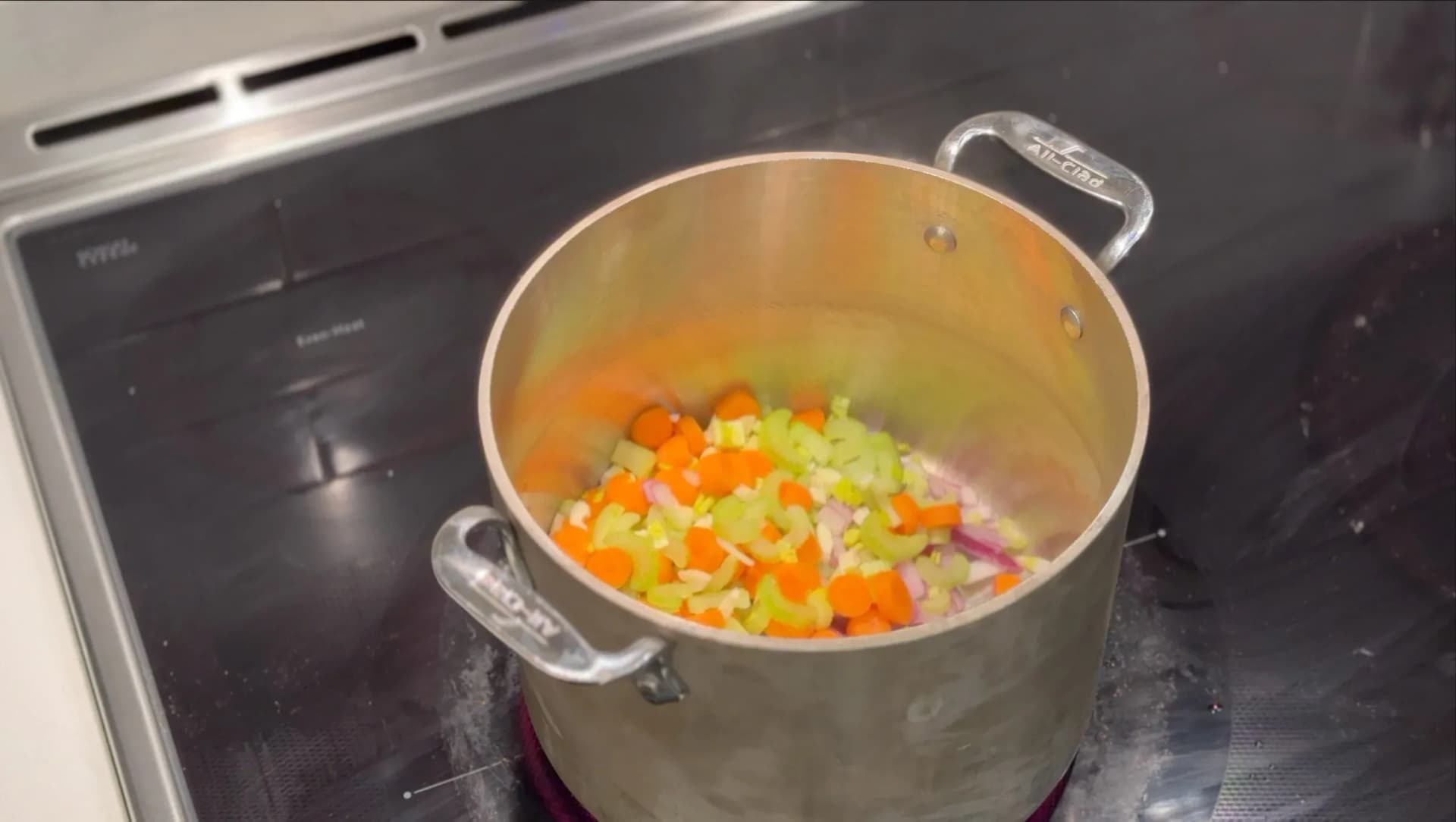 Large pot of diced celery, carrots, onions, and garlic sautéing in oil on stovetop for lobster broth base.