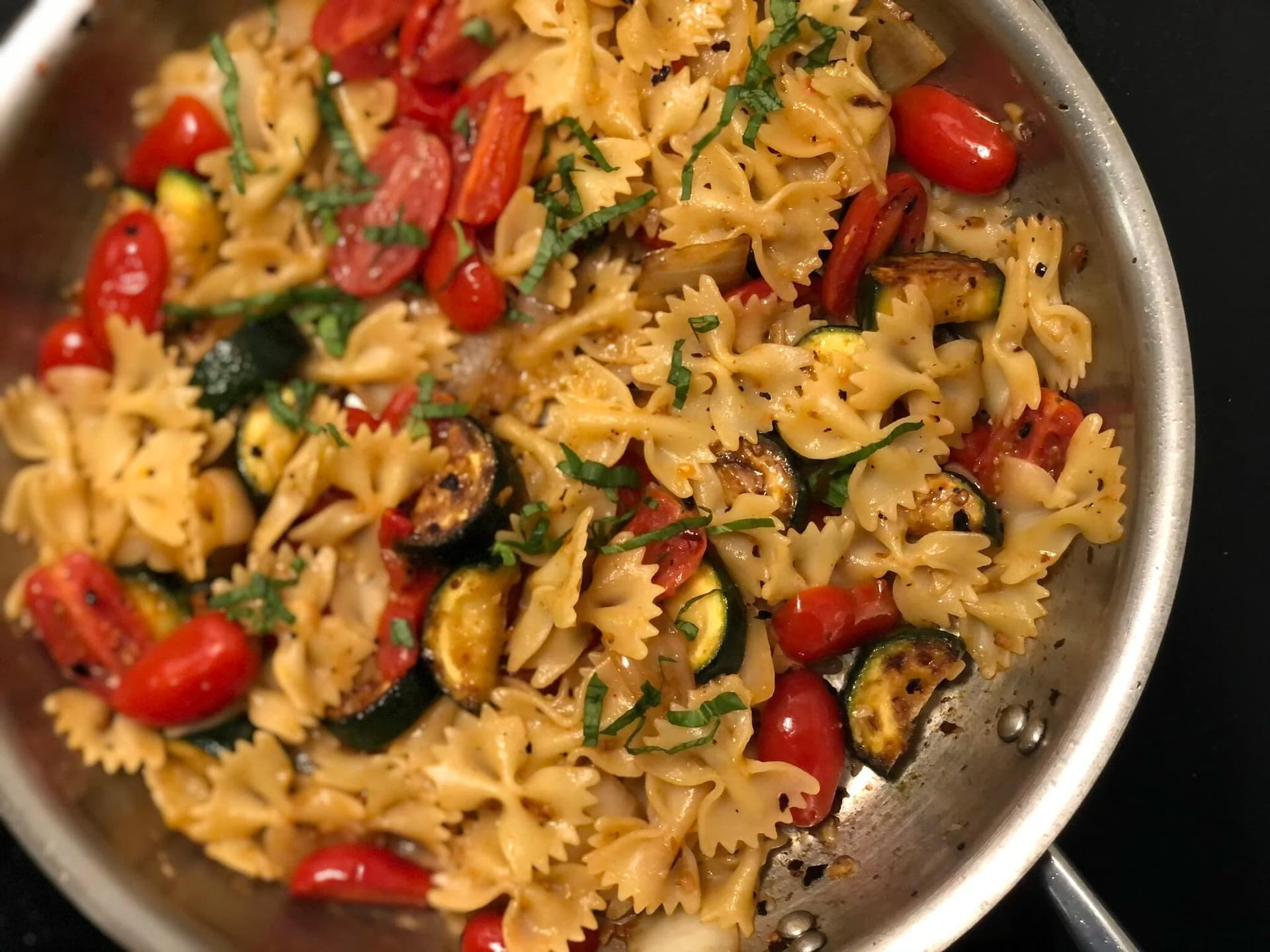 Mediterranean pasta with bow-tie noodles, sautéed zucchini, red bell peppers, and fresh basil in a skillet.