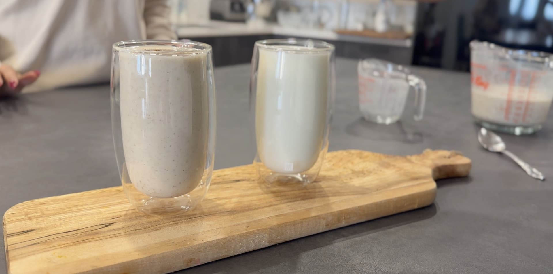 Two glasses of creamy sweet lassi served on a wooden board, one with visible spice garnish on top.