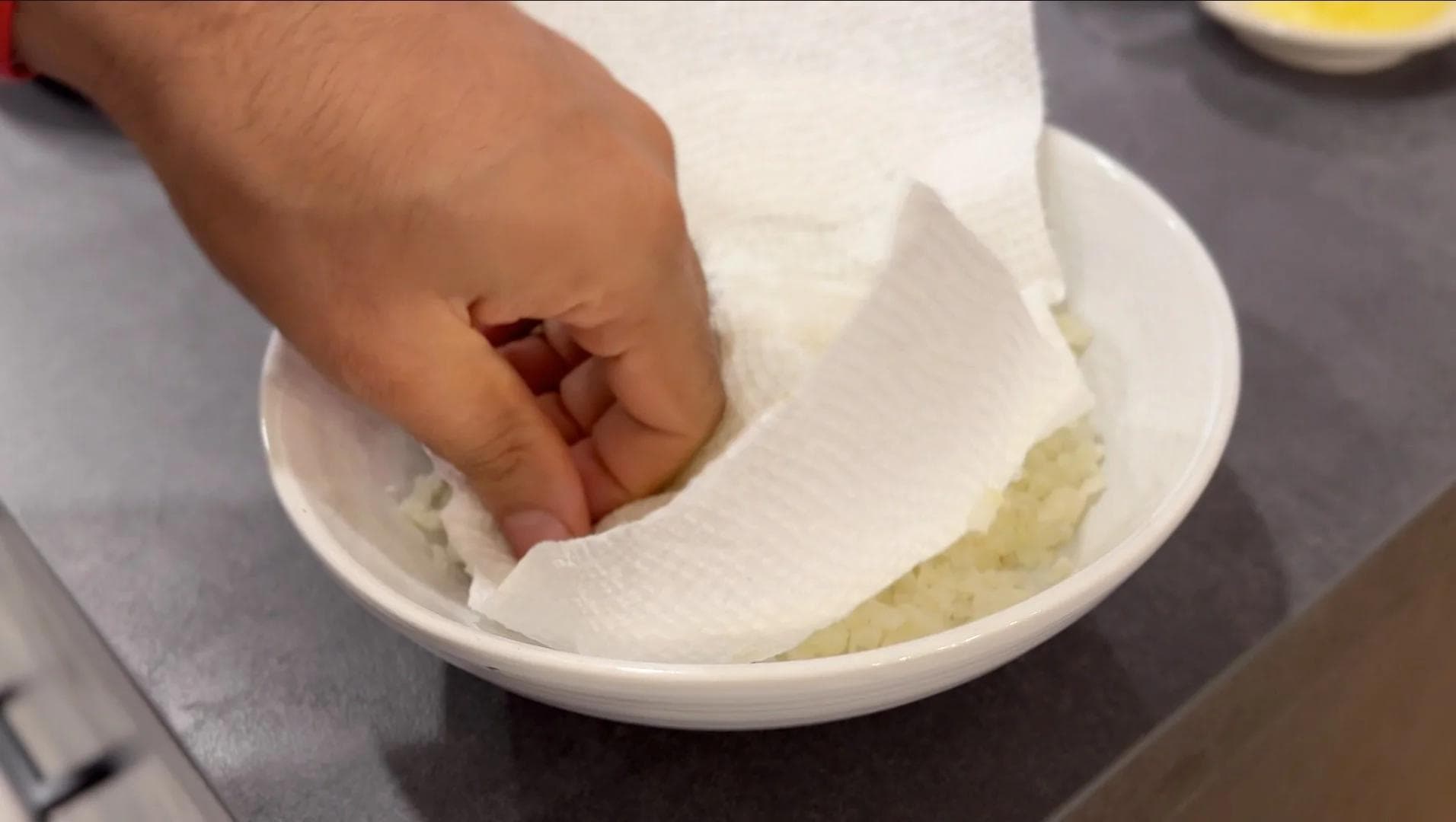 Hand pressing paper towel into bowl of riced cauliflower to remove excess moisture.