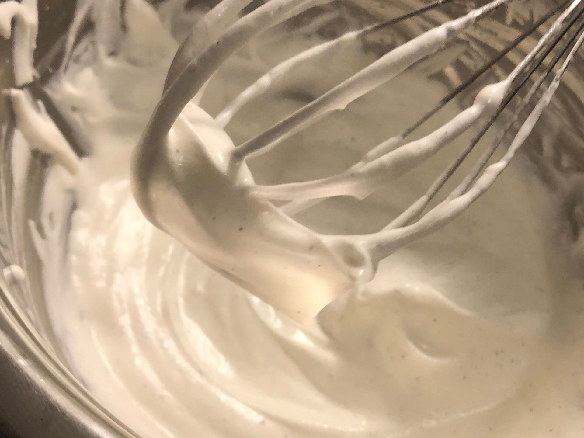 Whipped cream with soft peaks being lifted on a whisk during hand-whisking process.