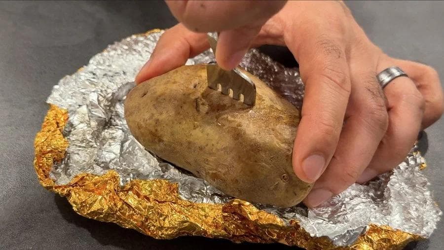 Hand holding a soft-skinned baked potato wrapped in foil, demonstrating air fryer texture without foil wrapping.