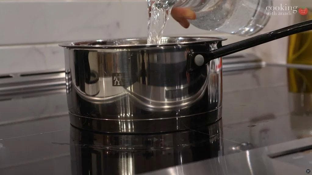 Water being poured into a stainless steel pot on a stovetop for cooking steel-cut oats.