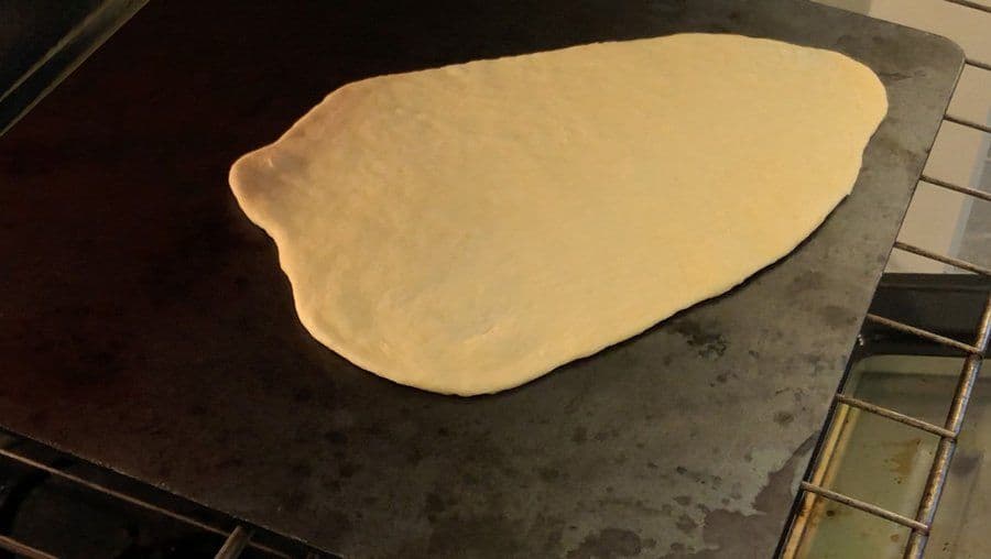 Rolled dough stretched into an oblong shape on a dark pizza steel, ready for broiling.