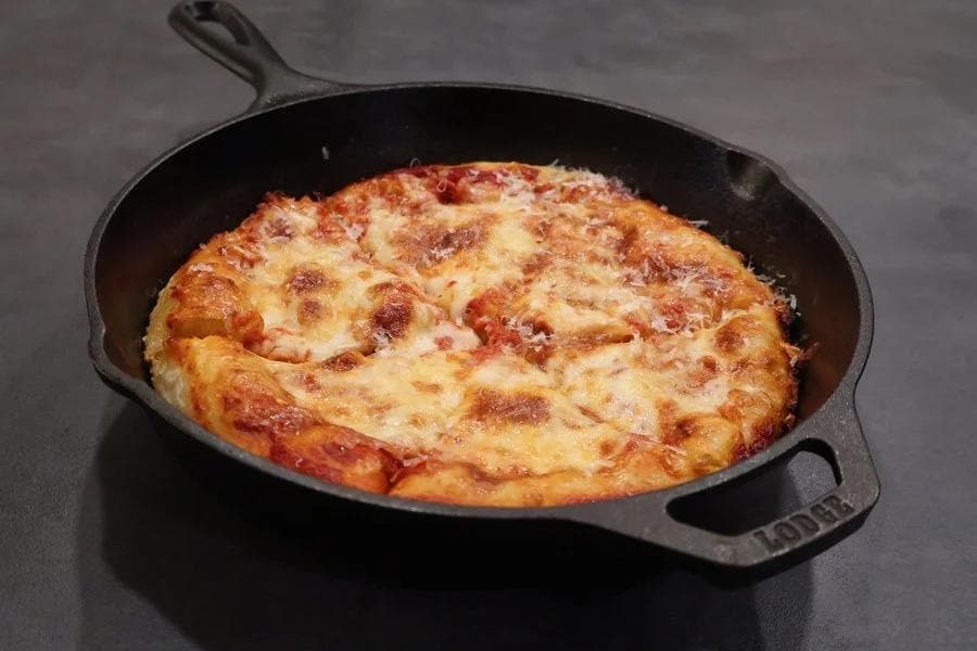 Golden-brown cast iron skillet pizza with crispy edges and melted cheese topping.