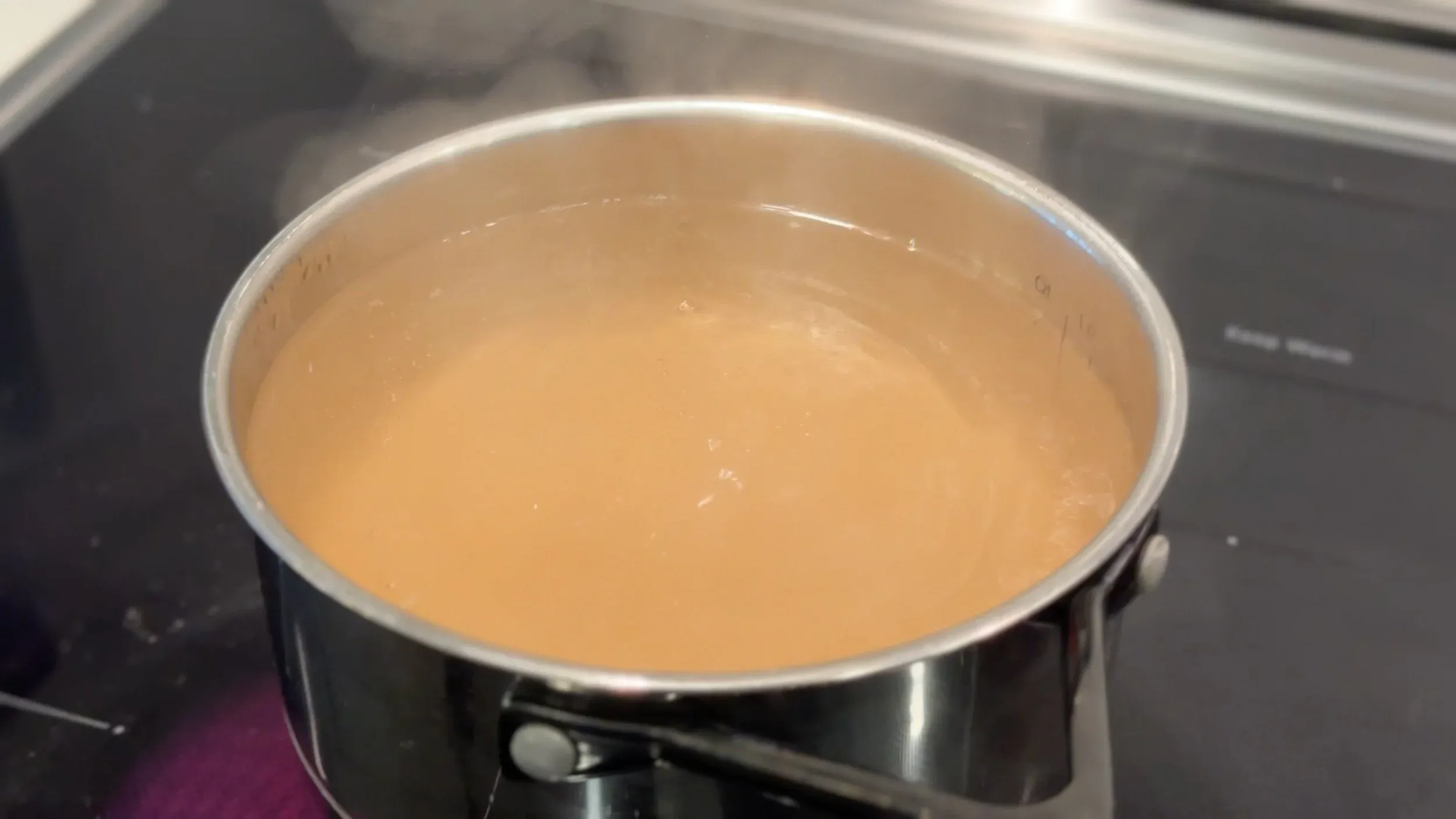 Boiling pickling liquid in a stainless steel pot on a stovetop, showing a clear amber-colored brine.