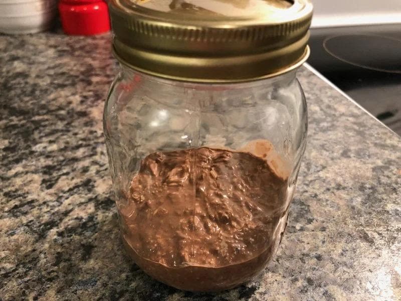 Mason jar filled with chocolate overnight oats mixture, sealed with a gold lid, sitting on a granite countertop.