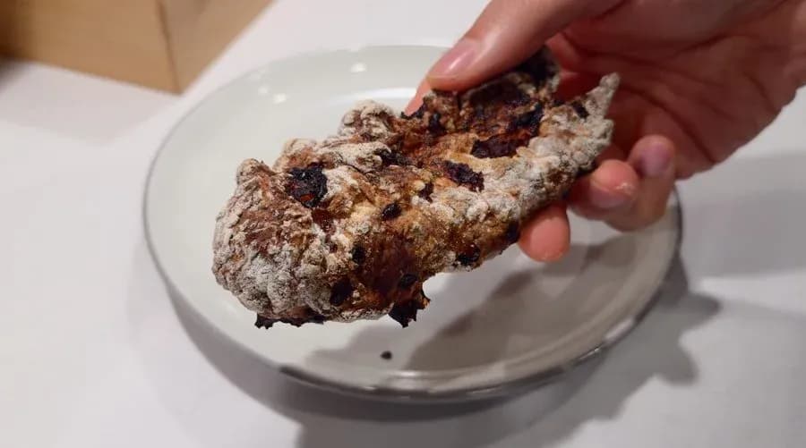 Breading falling off an air fryer chicken tender held over a white bowl, showing improperly coated, unevenly browned chicken.