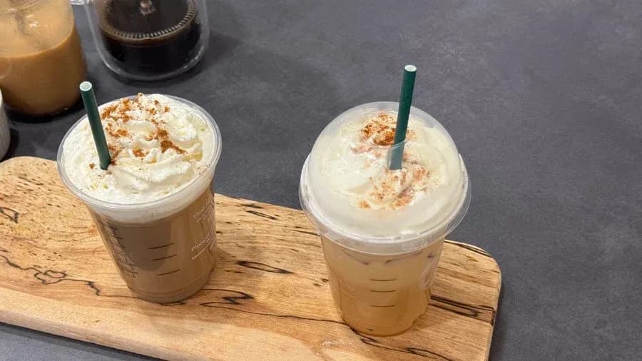 Two iced pumpkin spice lattes with whipped cream and cinnamon sprinkles on a wooden board.