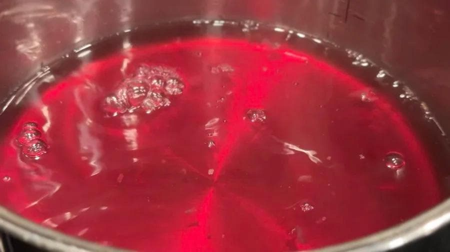 Rose petals simmering in pink-tinted water in a stainless steel saucepan.