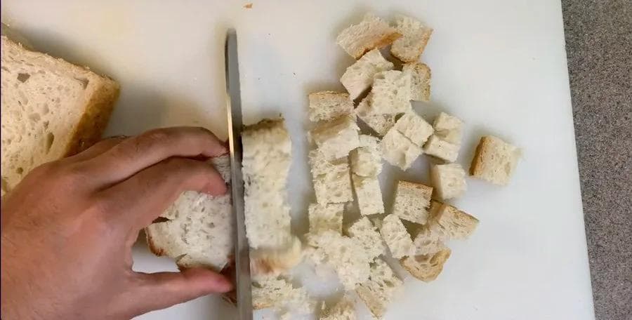 Hand cutting soaked bread into cubes on a white plate for Indian chicken cutlets.