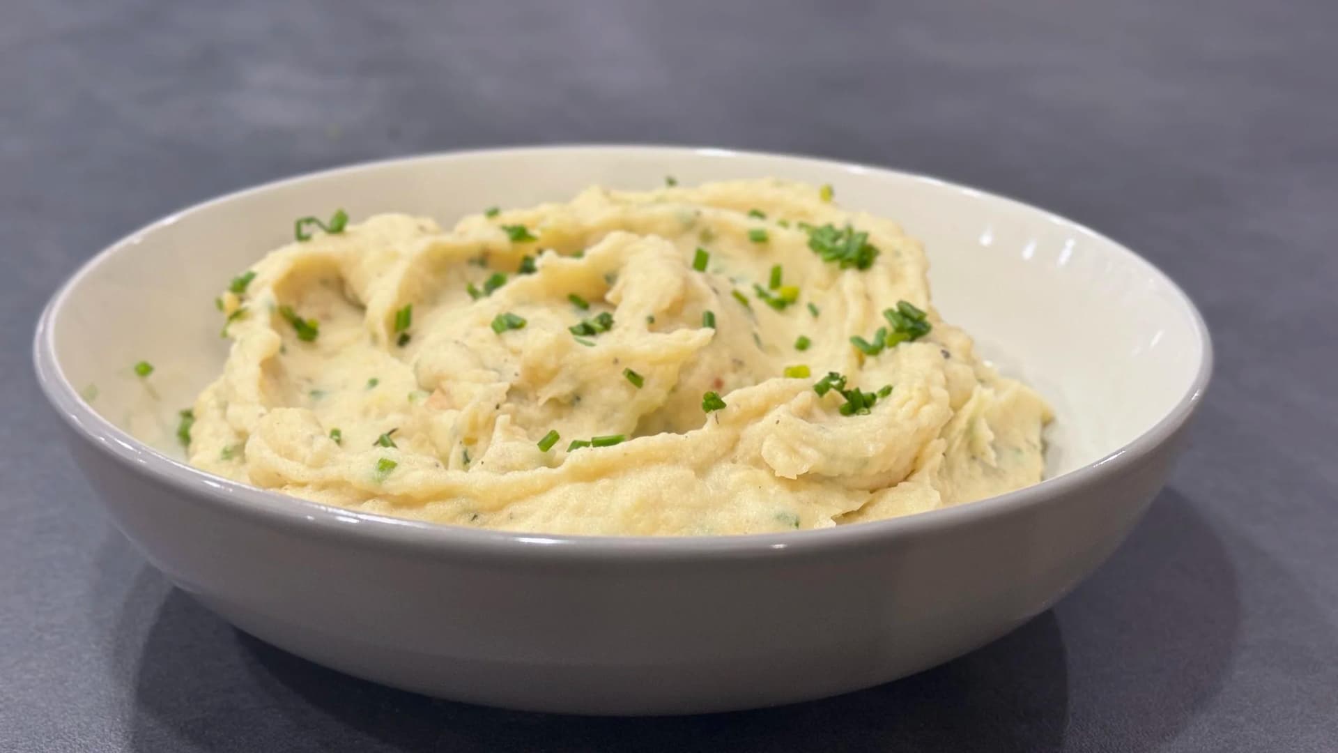 Creamy garlic-herb mashed potatoes garnished with fresh chives in a white bowl.