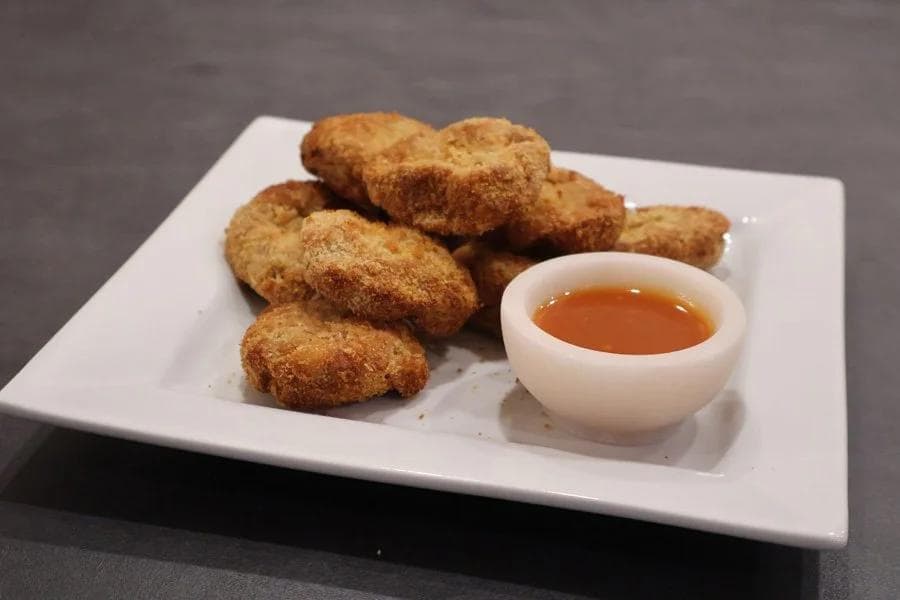 Golden-brown air fryer chicken nuggets on a white plate with a small bowl of dipping sauce.