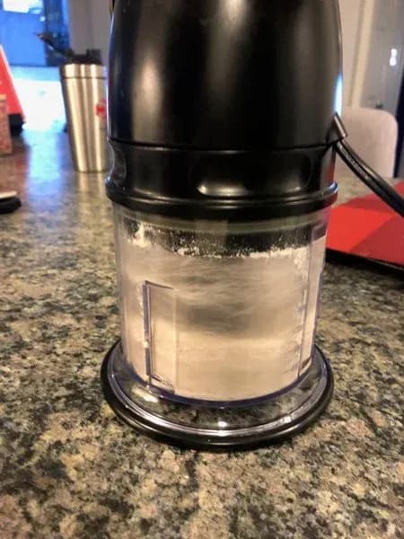 Clear container filled with no-bake protein cookie dough mixture on granite countertop.