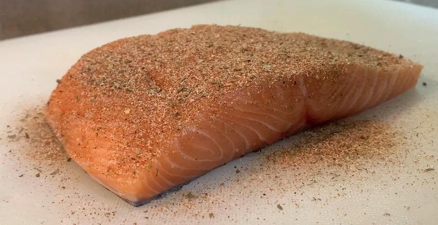Salmon fillet with blackened spice crust on white plate, skin side down.