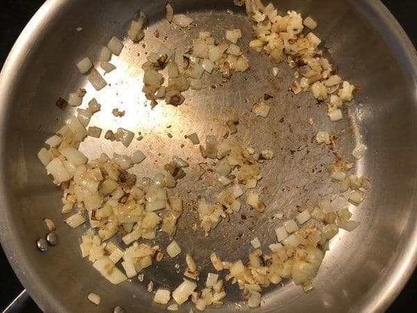 Diced onions and minced garlic sautéing in olive oil in a stainless steel pan.