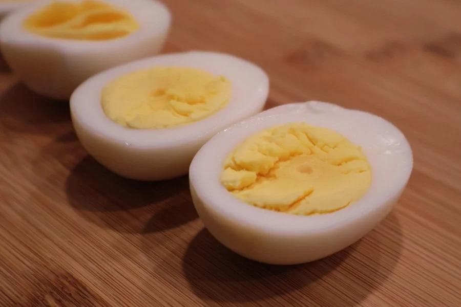 Three halved hard boiled eggs with bright yellow yolks on a wooden surface.