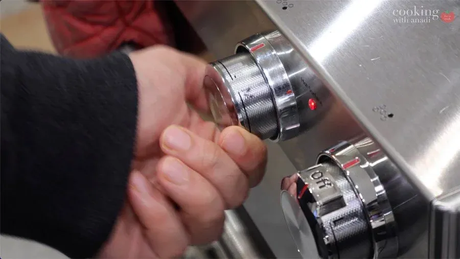 Hand adjusting temperature dial on stainless steel stovetop burner to medium heat.