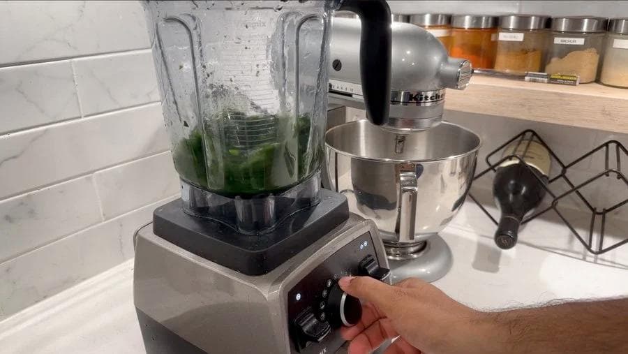 Hand blending blanched spinach with water in a food processor on high speed.